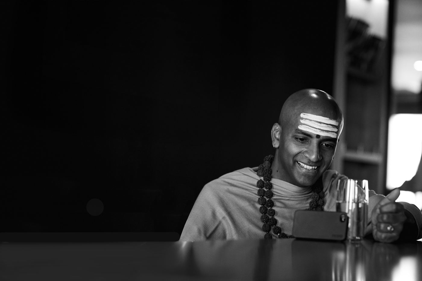 Dandapani seated at a table in low light, smiling, his attention entirely on the person he is with.