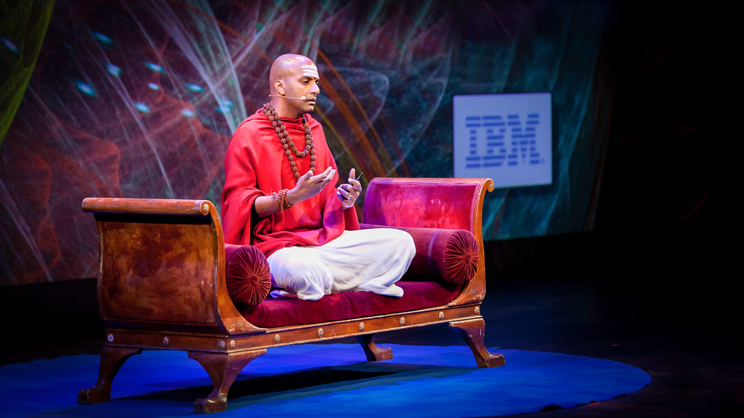 Dandapani mid-keynote on a darkened stage, addressing a corporate audience