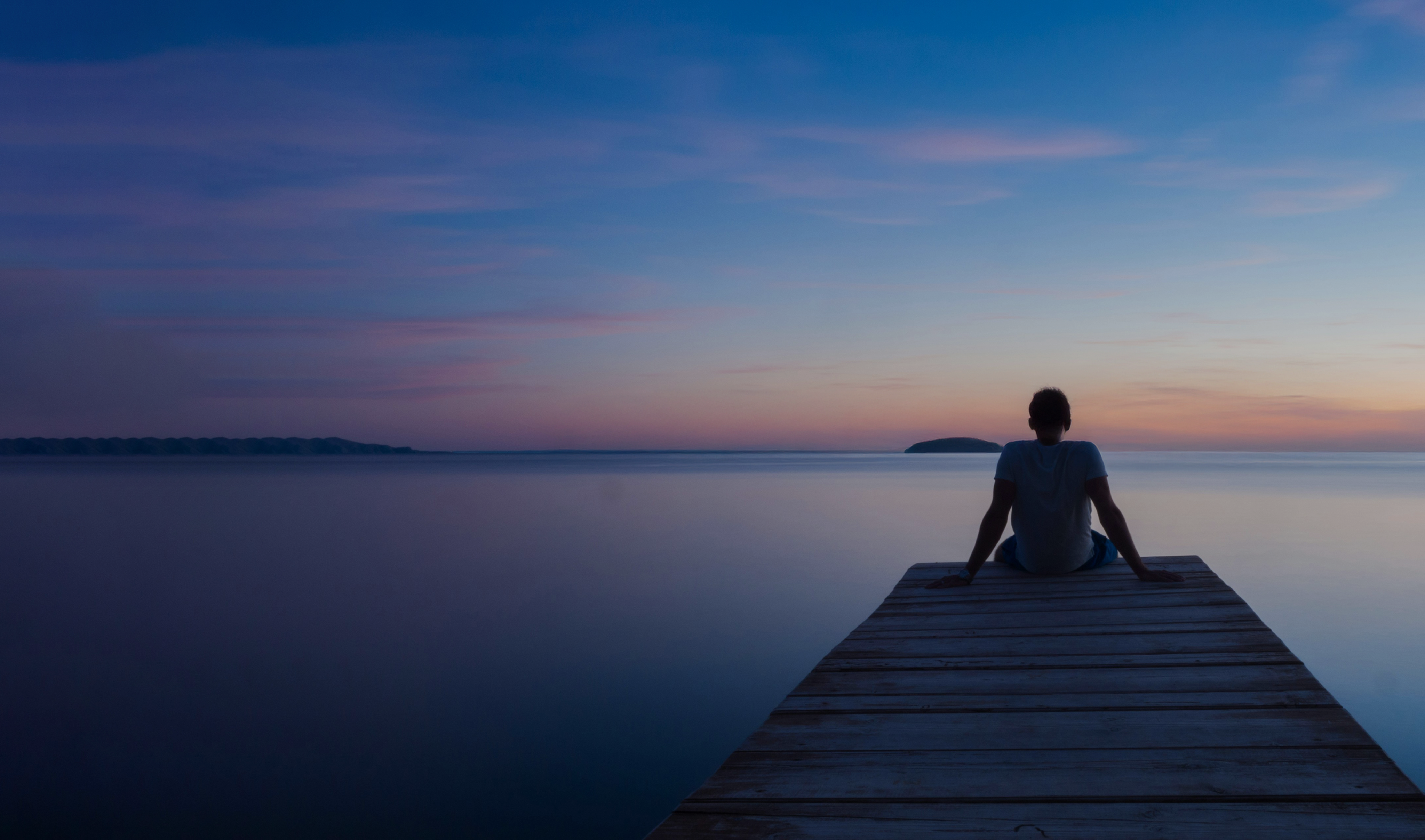 Person sitting calmly on a pier at sunset, symbolizing clarity and focus.