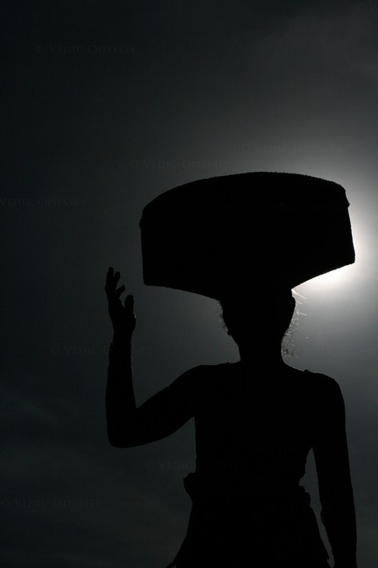 A Balinese lady goes about her day, carrying a basket on her head with groceries purchased at a local market. Ubud, Bali. 