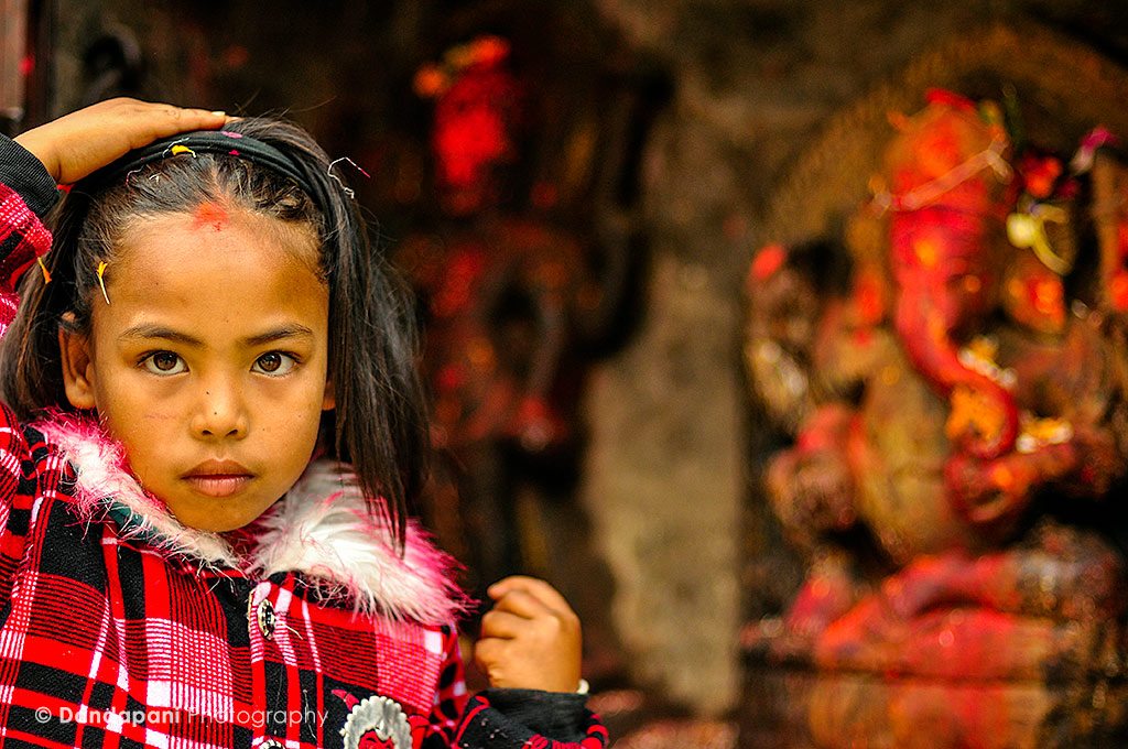 A young girl prays to a statue of Ganesha at a small shrine in Kathmandu, Nepal. 