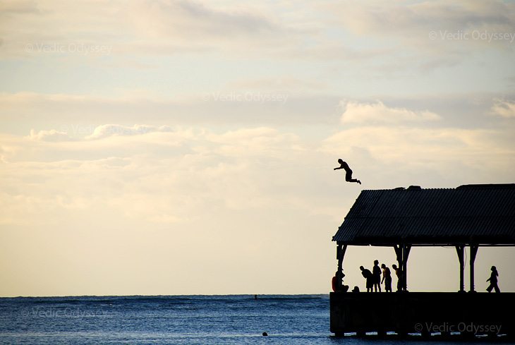 A young boy jumps off a roof at the end of a long pier in Hanalei Bay, Kauai, Hawaii.
