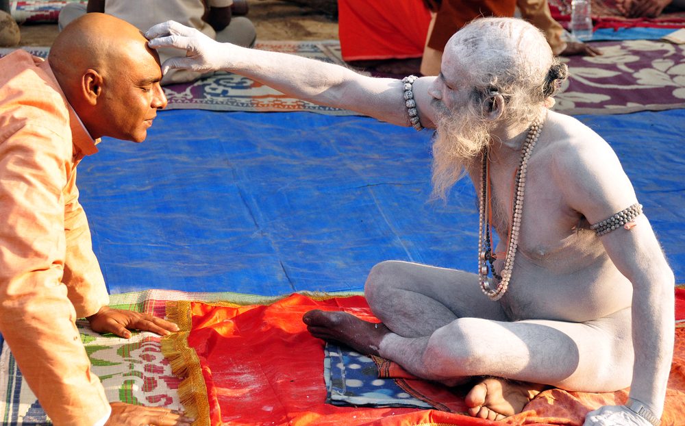 A Hindu pilgrim seeks blessings from a Naga sadhu, smeared in ashes and adorned with rudraksha beads.