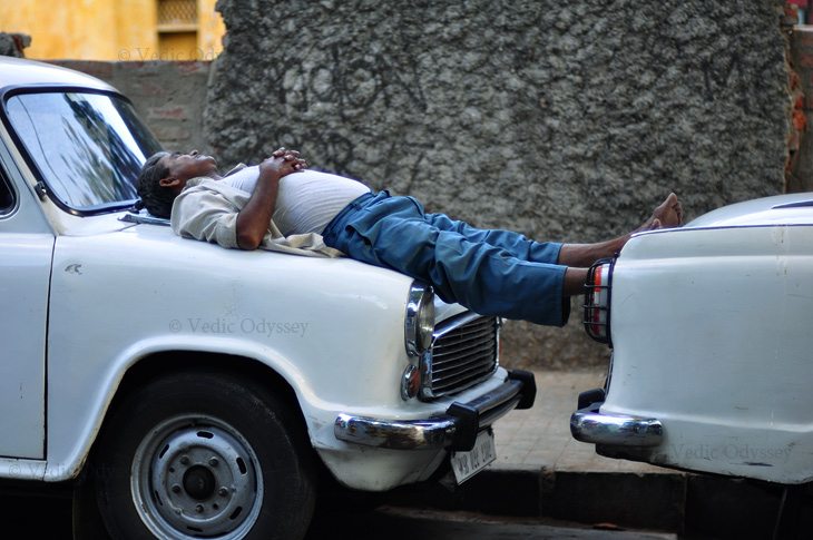 A taxi driver takes a nap on his taxi in quiet alley way in the bustling city of Kolkata, India.
